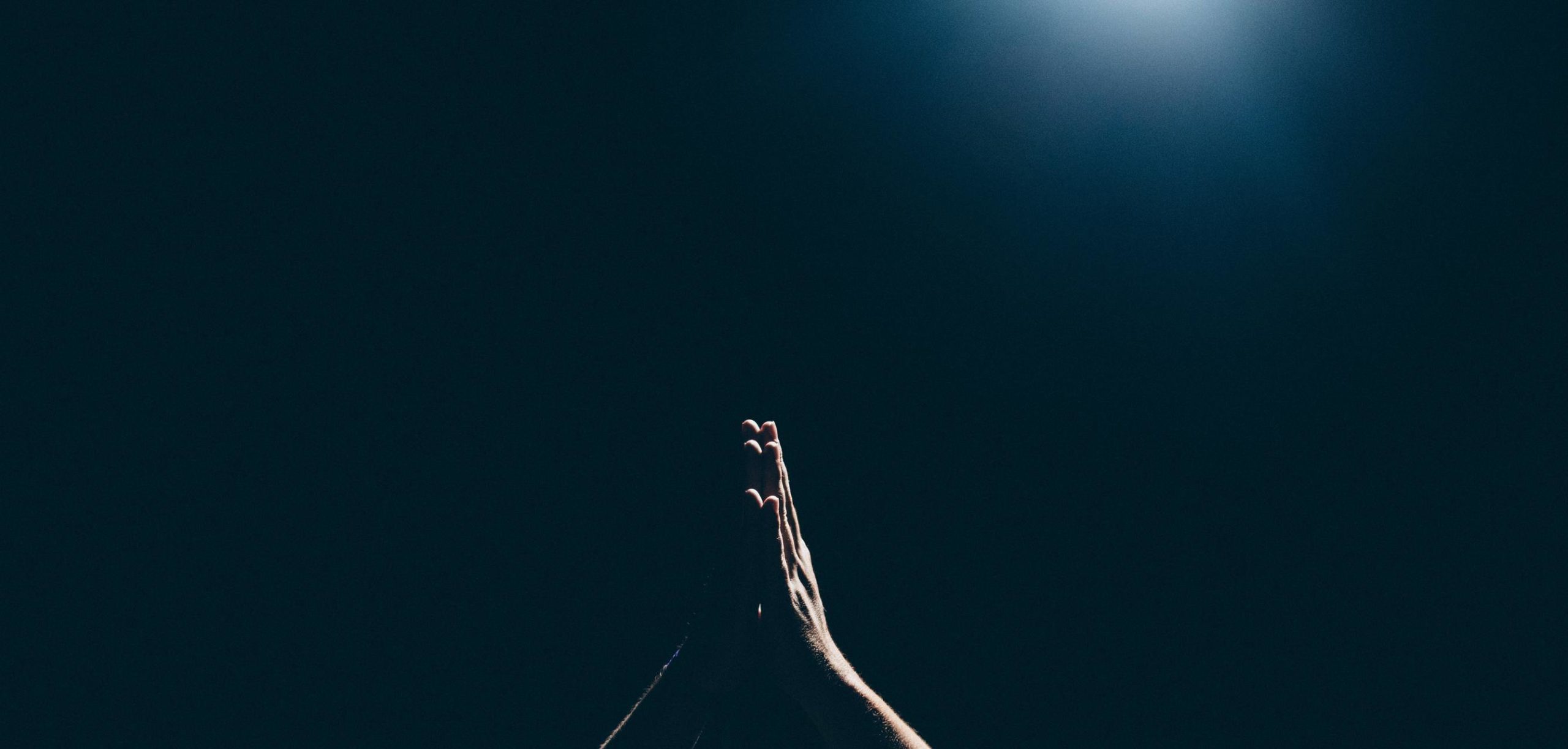 hands folded in prayer against a dark backdrop